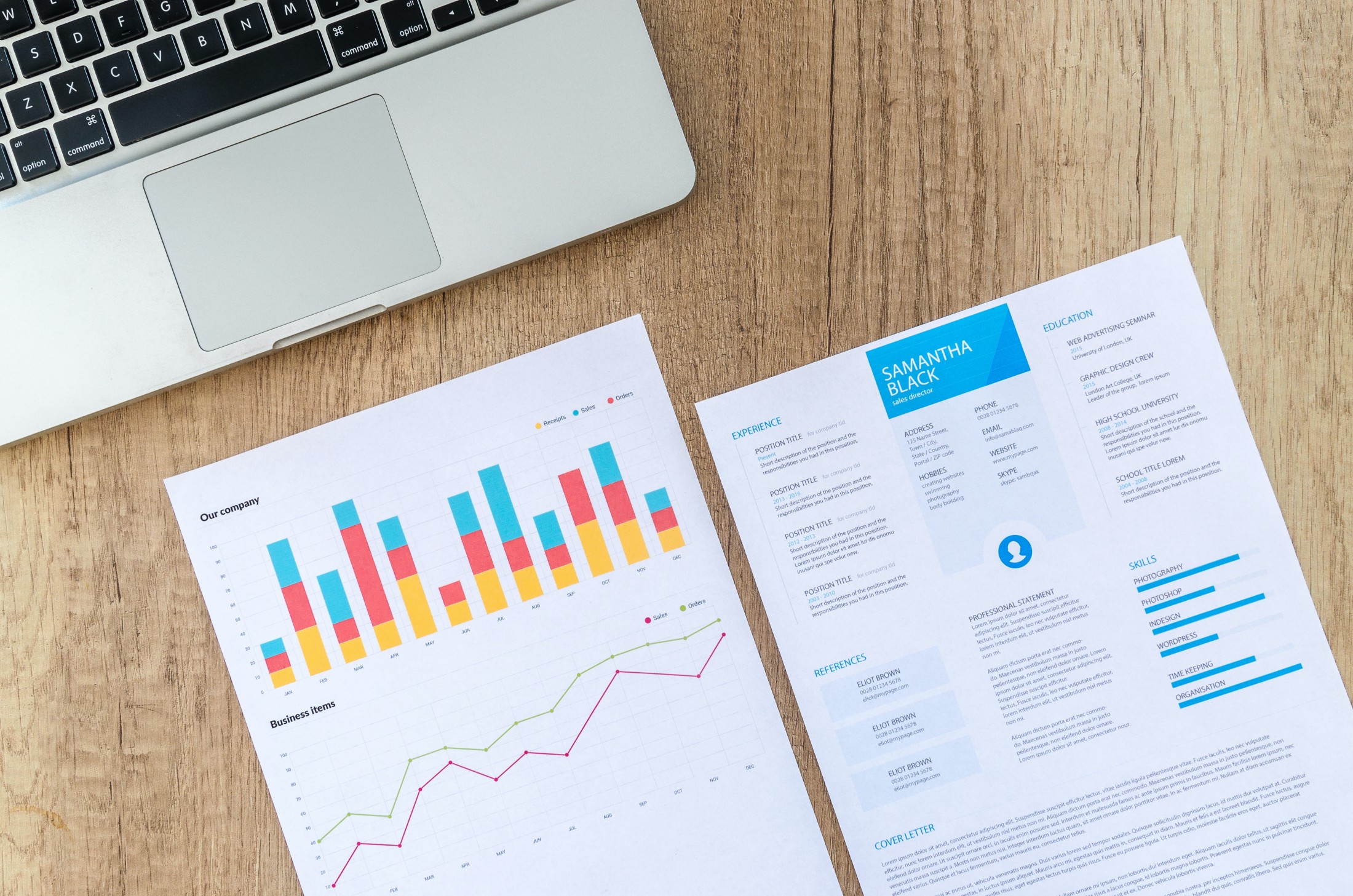 A wooden desk with a laptop, a colorful bar and line graph sheet, and a professional resume. The resume includes sections for experience, education, skills, and references.