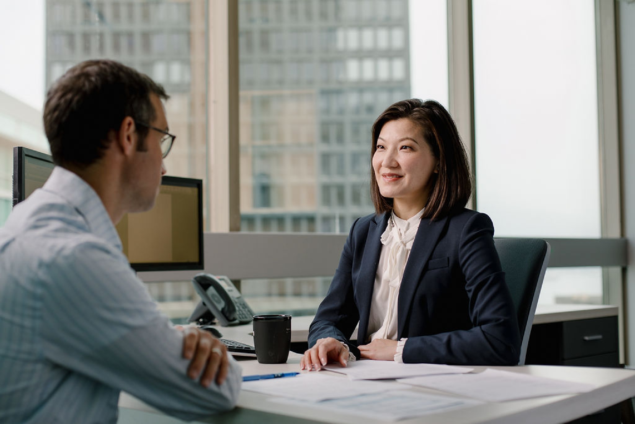 Woman in business attire sitting at office desk having a meeting with a male client.