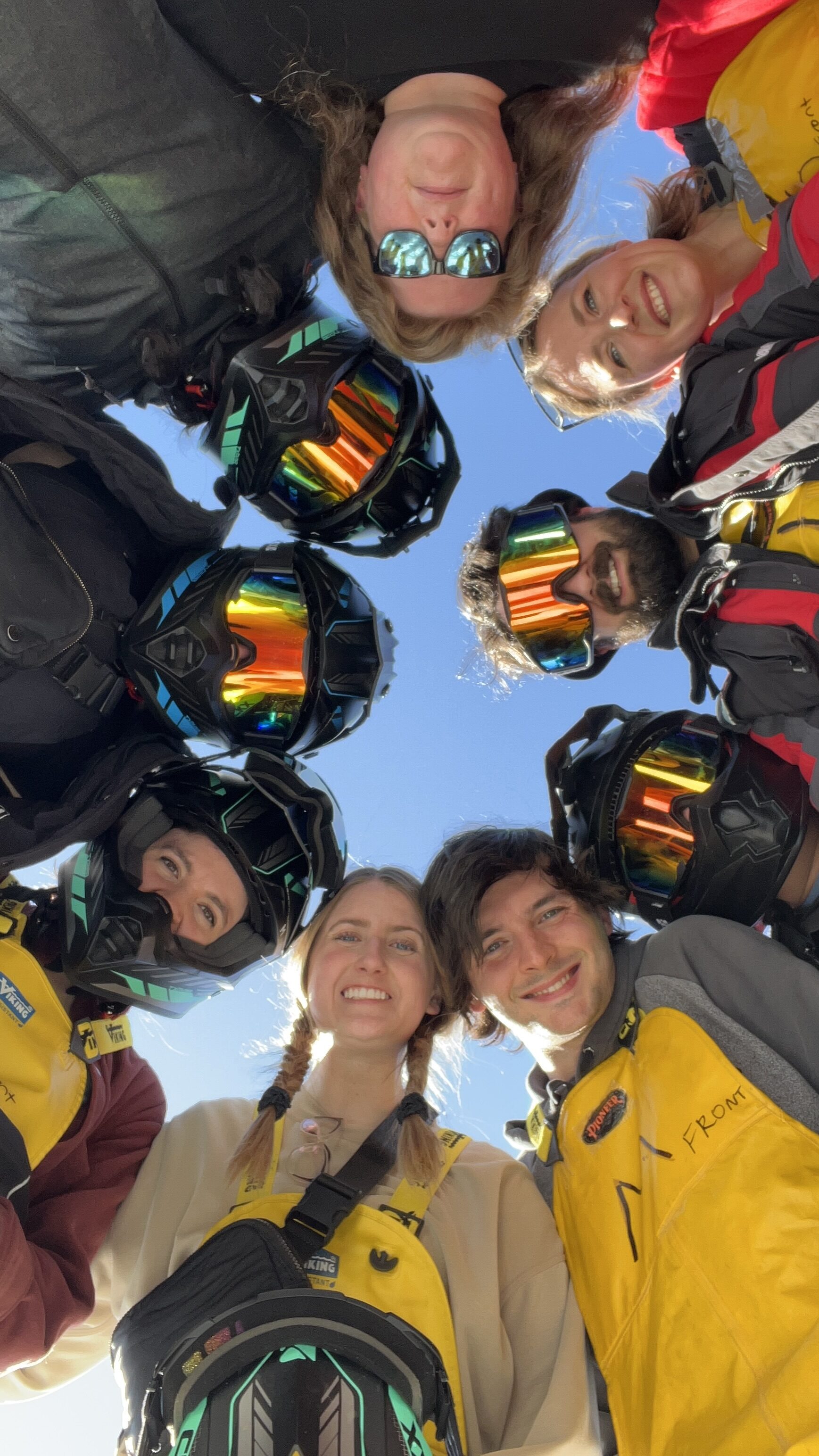 Array team in snow gear smiling for a group photo with their heads together in a circle.